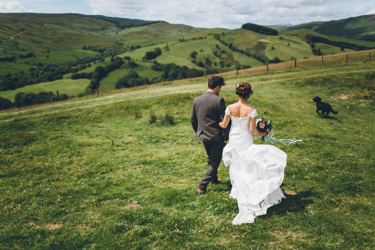 bride groom and dog running down hillside