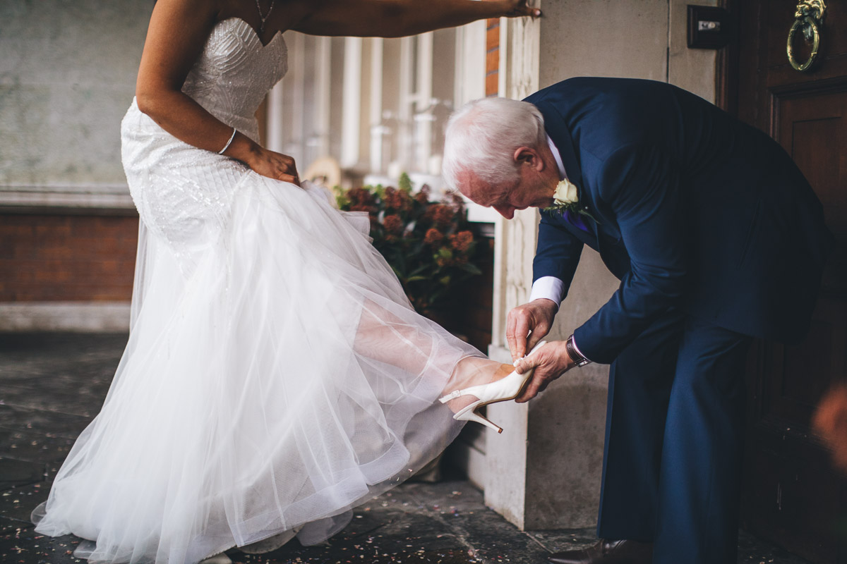 father of bride helps bride with shoes