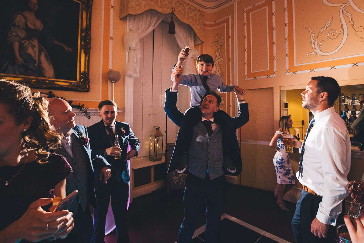 page boy dancing on fathers shoulders on the dance floor at the wedding reception