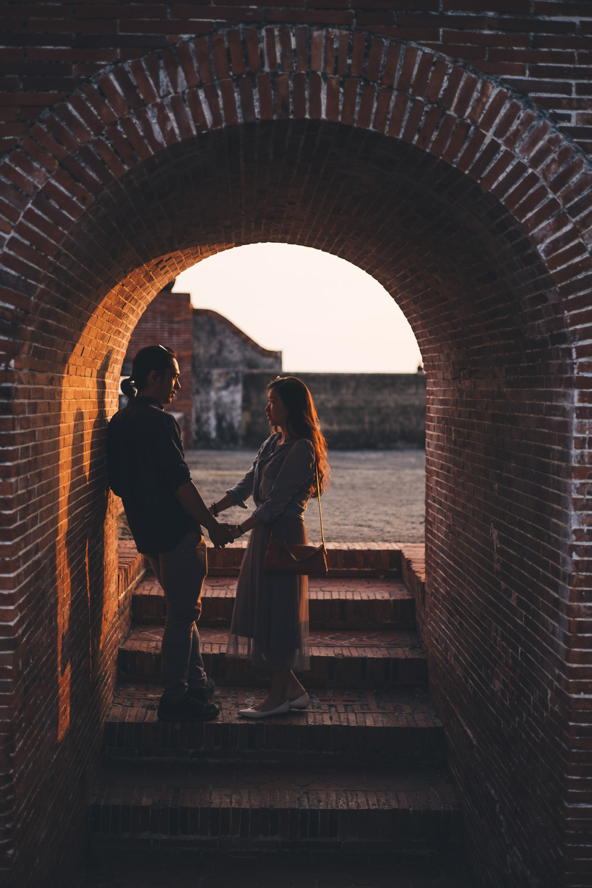 holding hands in an arch backlit by the sunset