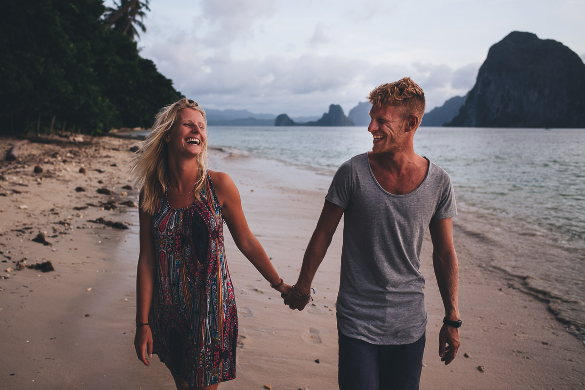 couple walking down the beach hand in hand laughing at each other