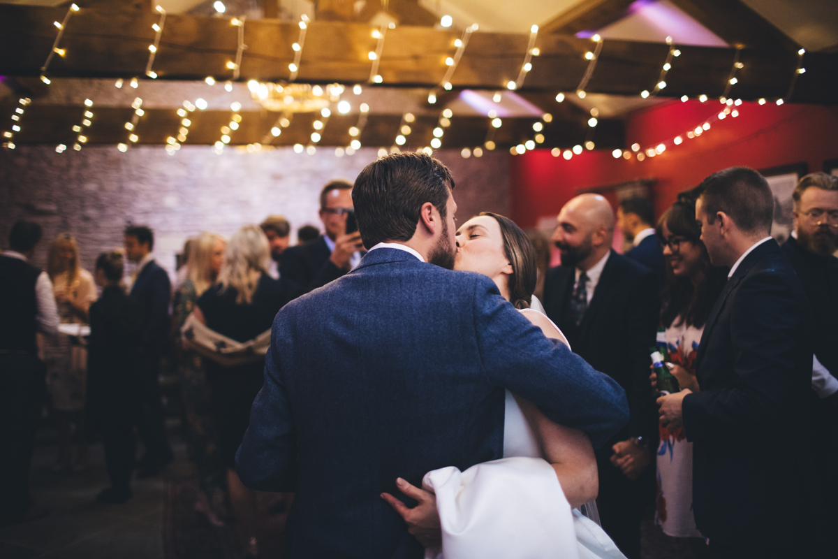 Bride and Groom kiss under fairy lit wooden beams