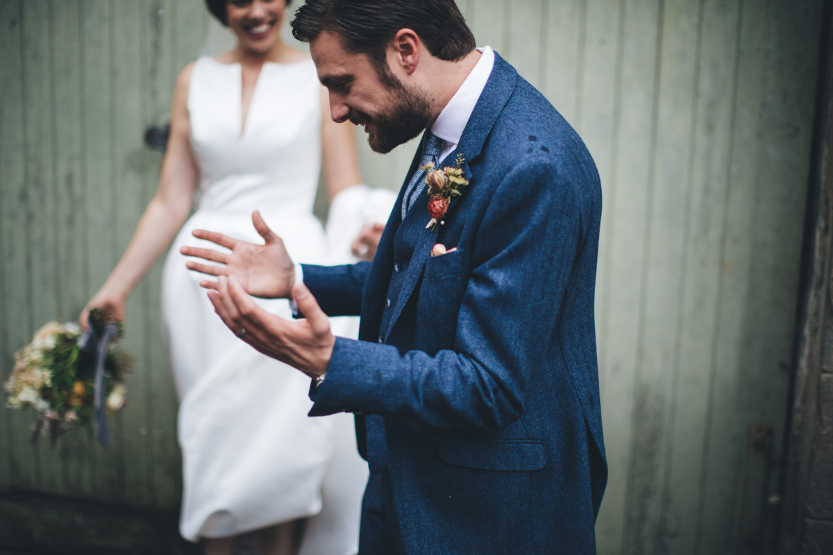 Groomin the foreground holding his hands out with the bride in the background smiling