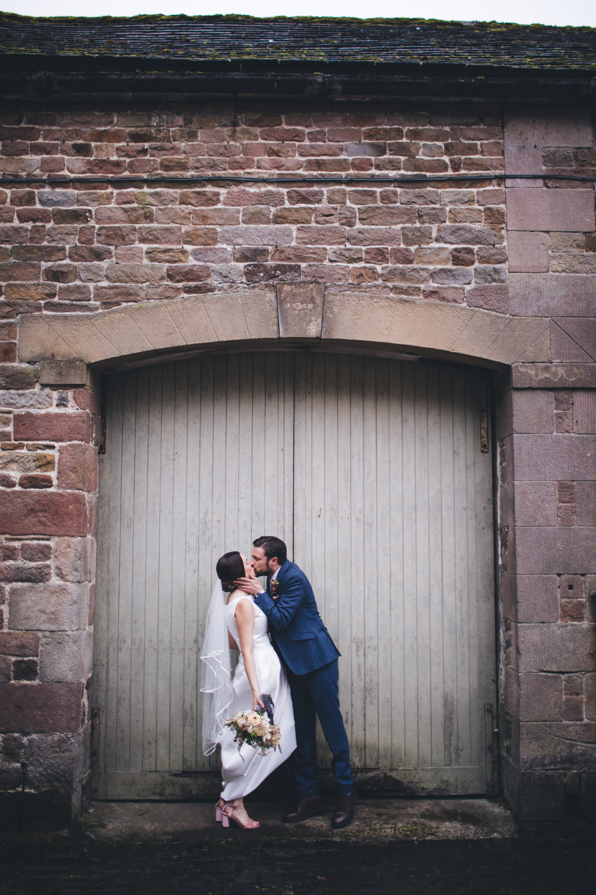 Bride and groom kiss in front of a large wooden doorway on a stone building