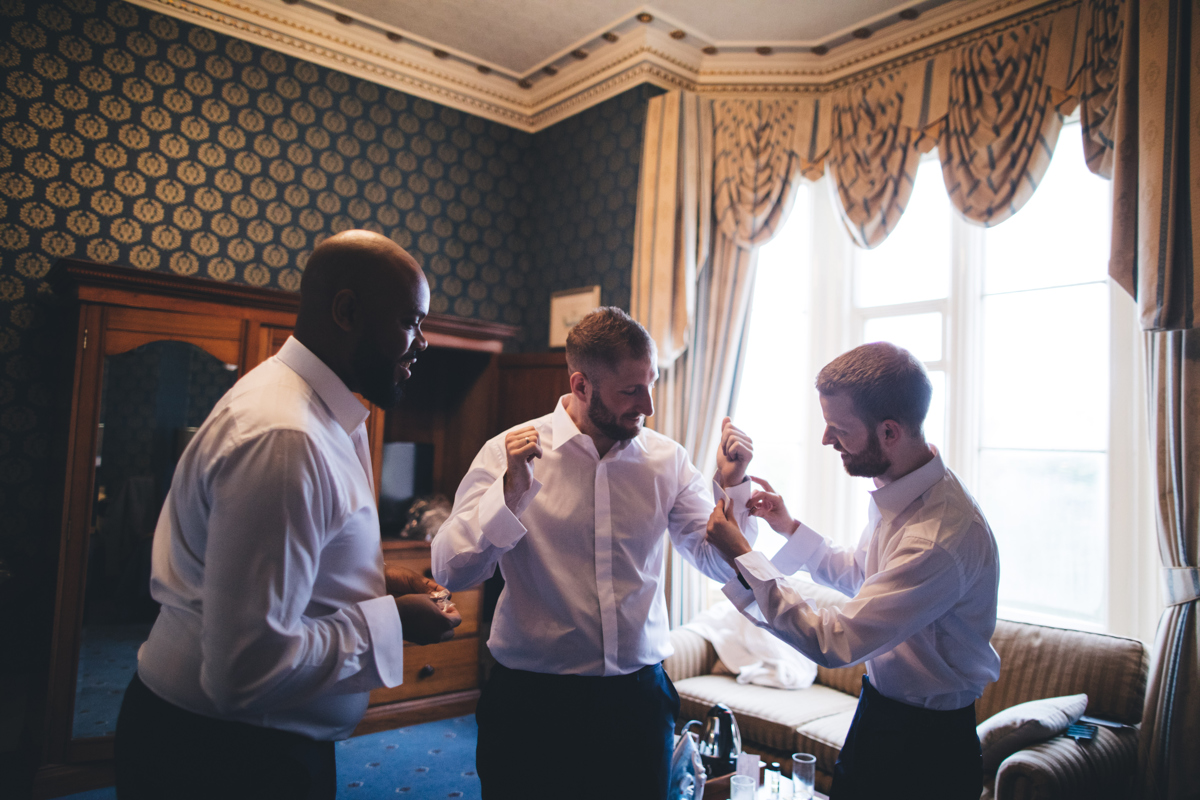 Groom getting his shirt on with the help of his groomsmen