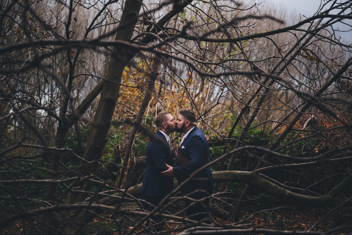 Two grooms kissing in woodland