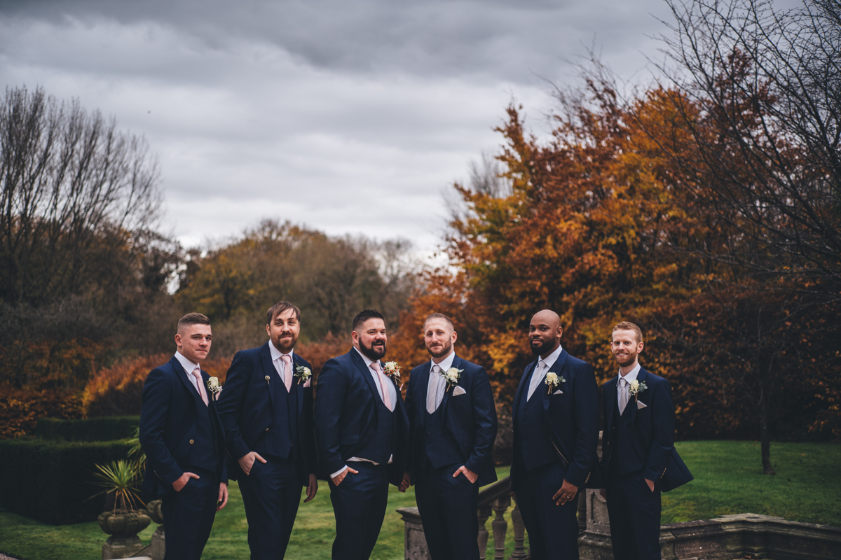 Two grooms with their four groomsmen in formal gardens