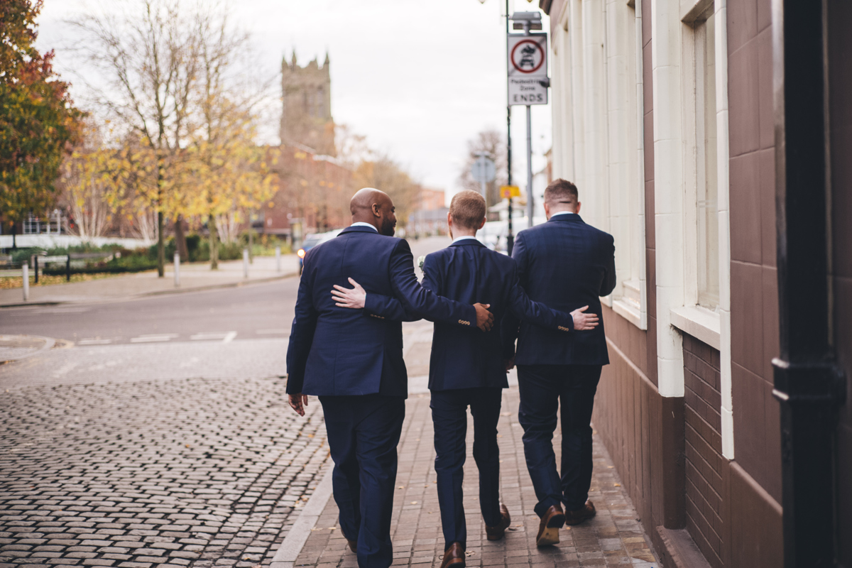 Three groomsmen walking away with their arms around each other