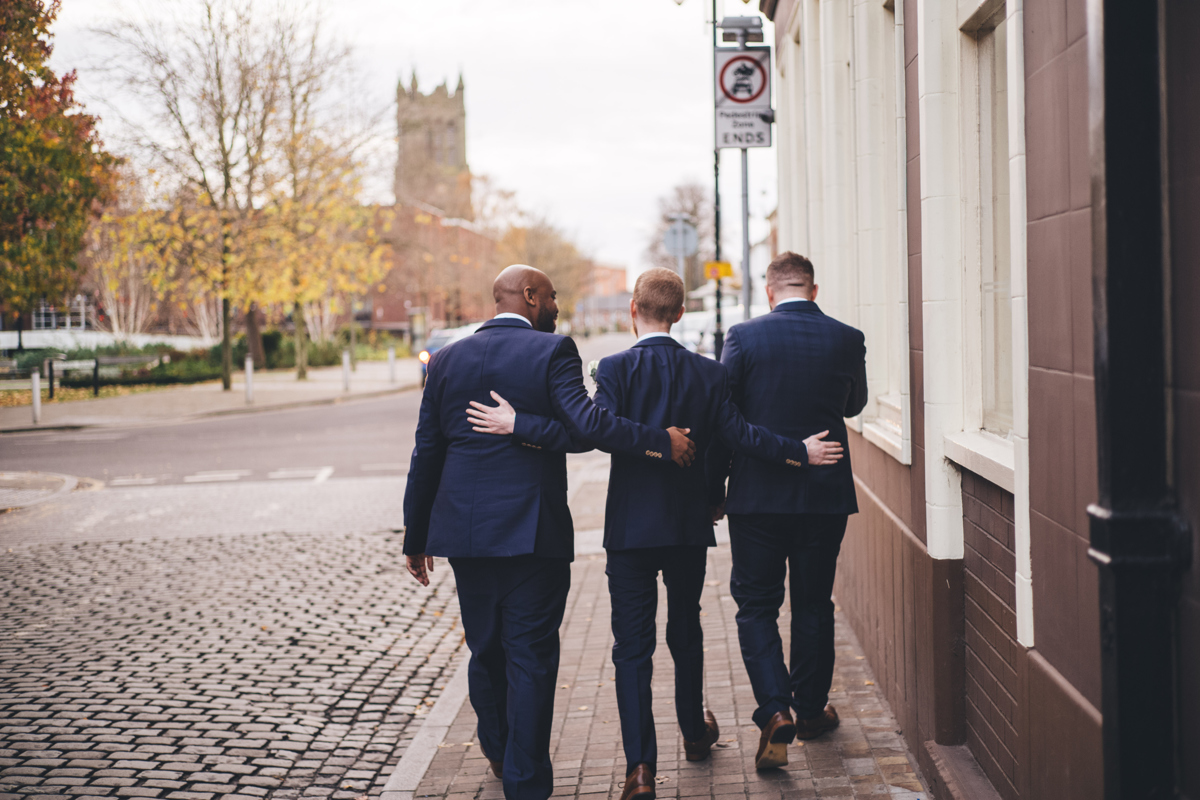 Three groomsmen walking away with their arms around each other