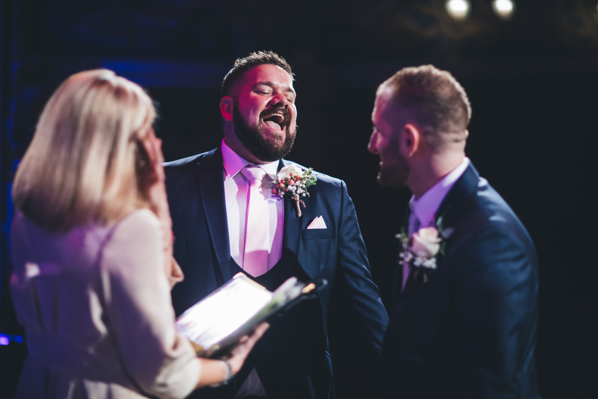 Two grooms laughing during their wedding ceremony