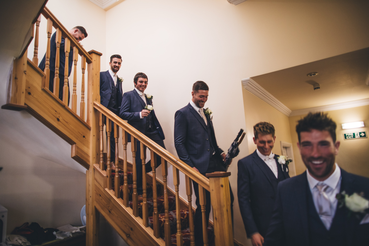 Five groomsmen and the groom walking down the stairs together in a line