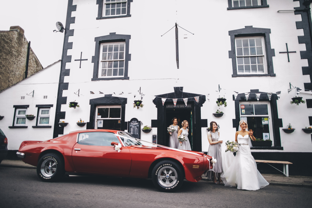 Bride and bridesmaids coming out of The Ship Inn pub with a red Pontiac car waiting outside