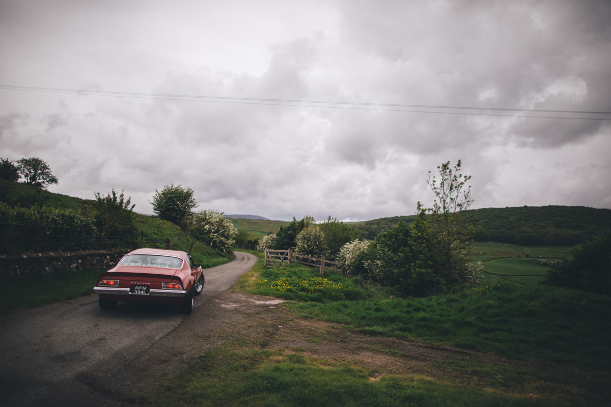 Countryside scene with a red Pontiac car driving off down a lane