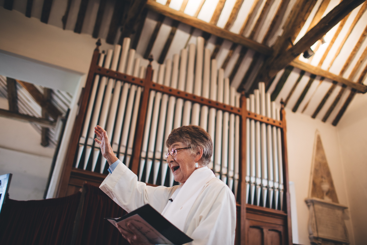 Female vicar doing a reading at the front of the church with her arm raised