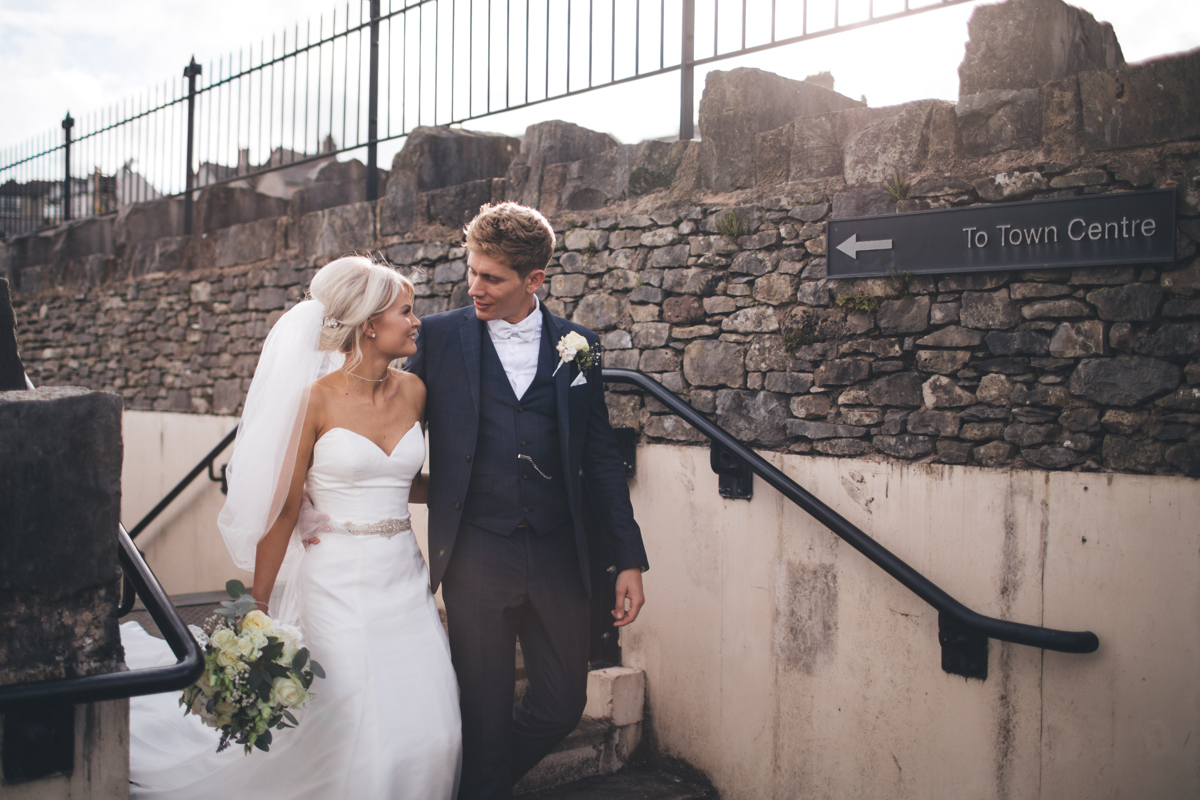 Bride and Groom walking down a short flight of stairs in front of a stone wall