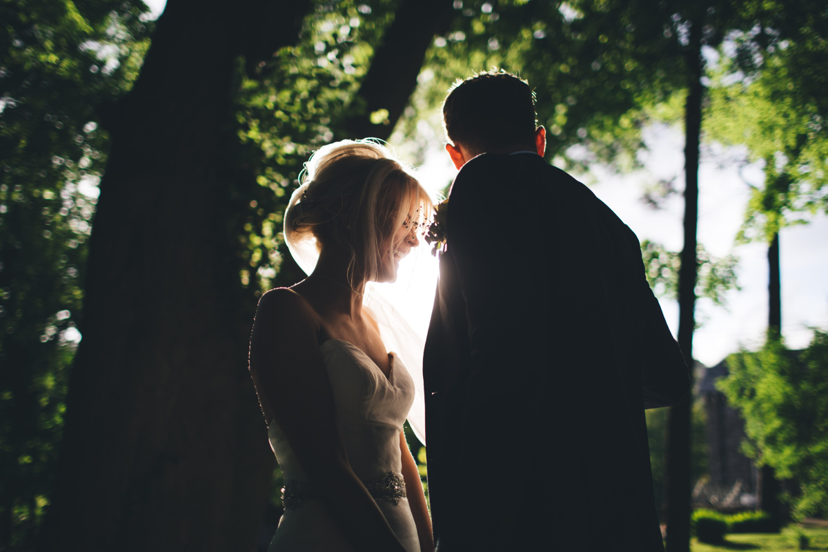 Bride and Groom stood facing each other with sunlight coming in through the trees