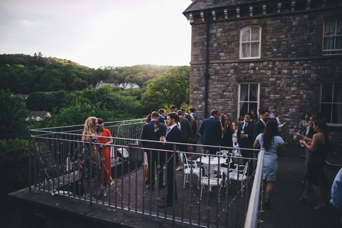 Wedding guests stood on a terrace outside at Grange hotel,Cumbria with views of trees and houses in the background