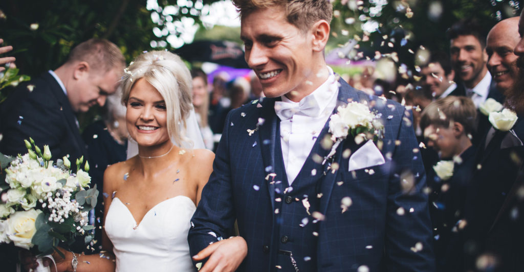 Bride and Groom walking arm in arm through a cloud of confetti with big smiles on their faces