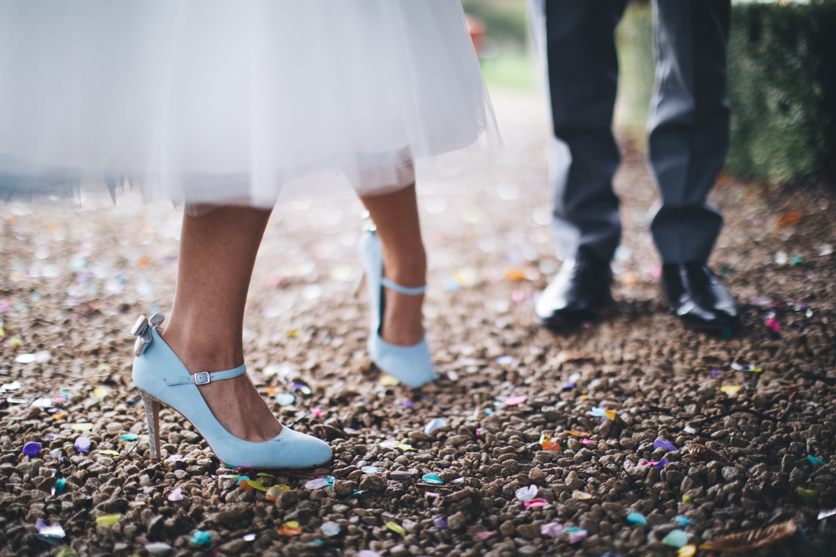 Bride's blue wedding shoes and Groom's black shoes in the background