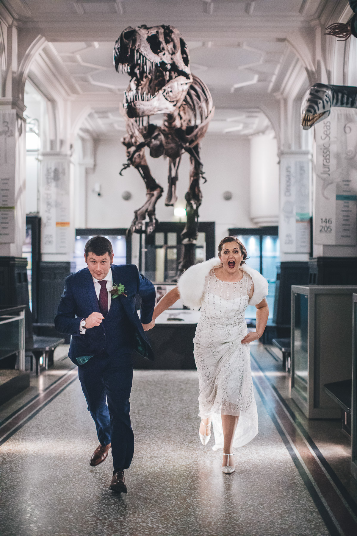 Bride and groom running away from a dinosaur skeleton