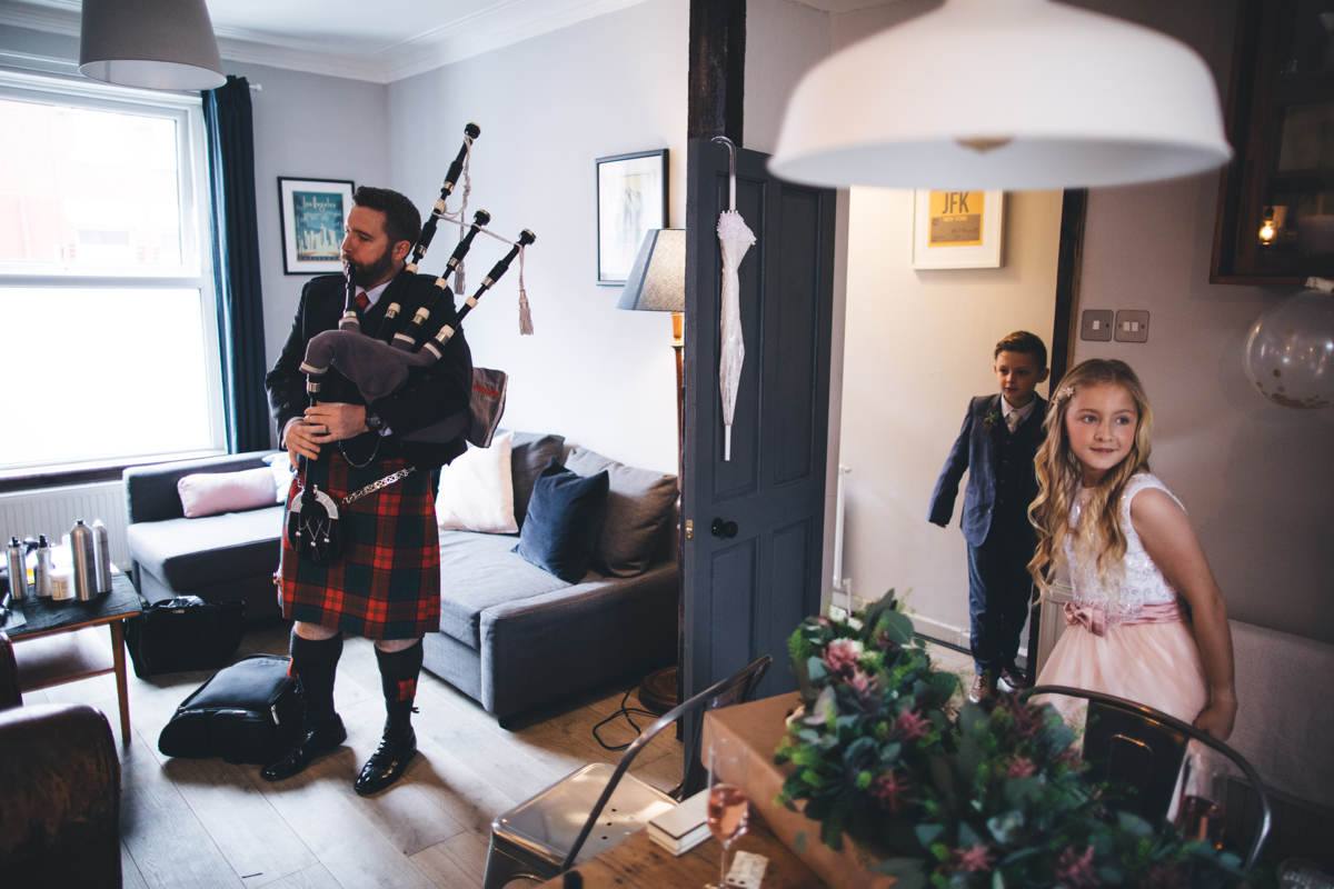 Bagpiper in kilt playing the bagpipes with young children in the room
