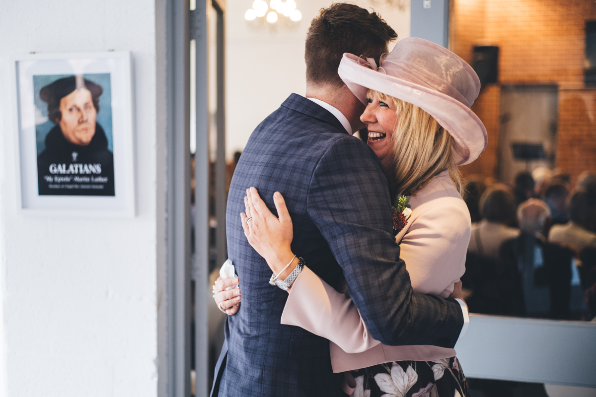 Groom hugging a female wedding guest wearing a hat