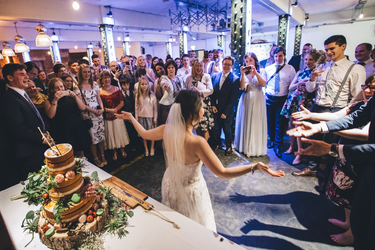 Bride with arms outstretched in front of the wedding cake with the wedding party looking on