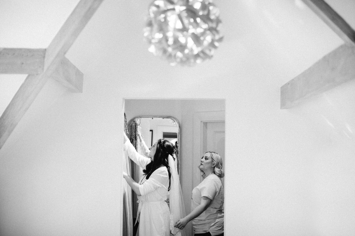 Black and white photograph through a doorway of bride getting ready next to a mirror