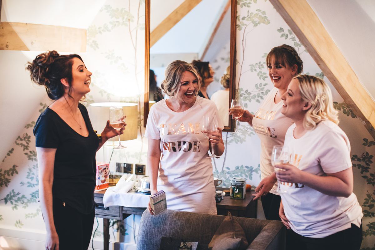 Bridesmaids wearing 'Team Bride' T-Shirts holding glasses of wine and laughing