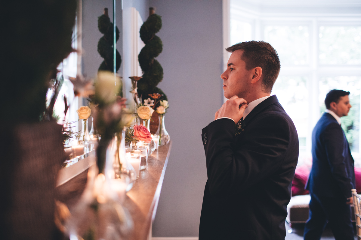 Groom adjusting his collar in the mirror