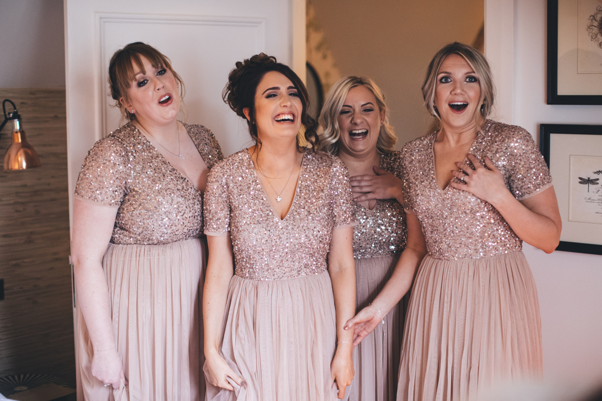 Four bridesmaids smiling and looking shocked as they see the bride who is out of shot