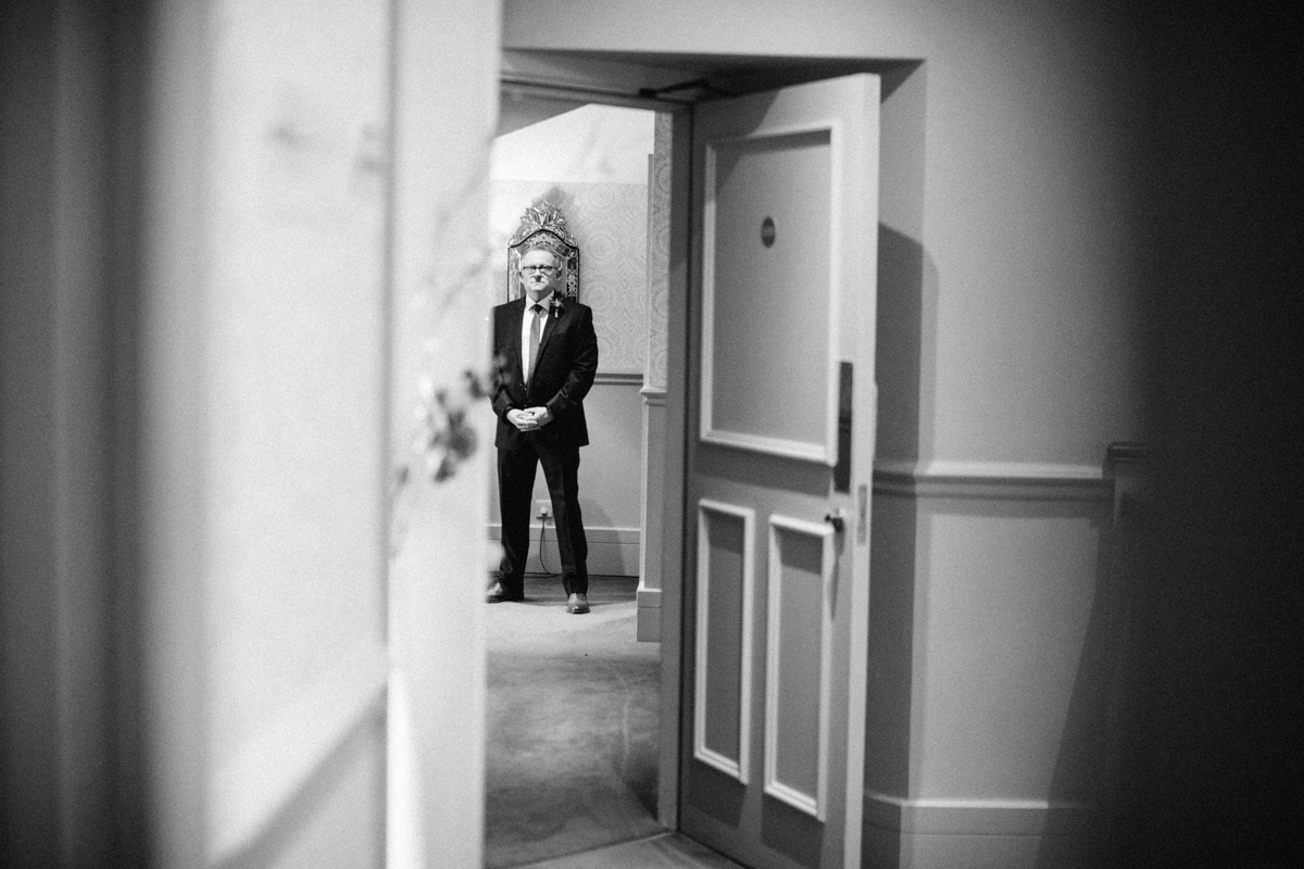 Father of the bride wearing a suit photographed in the corridor of a hotel through a doorway