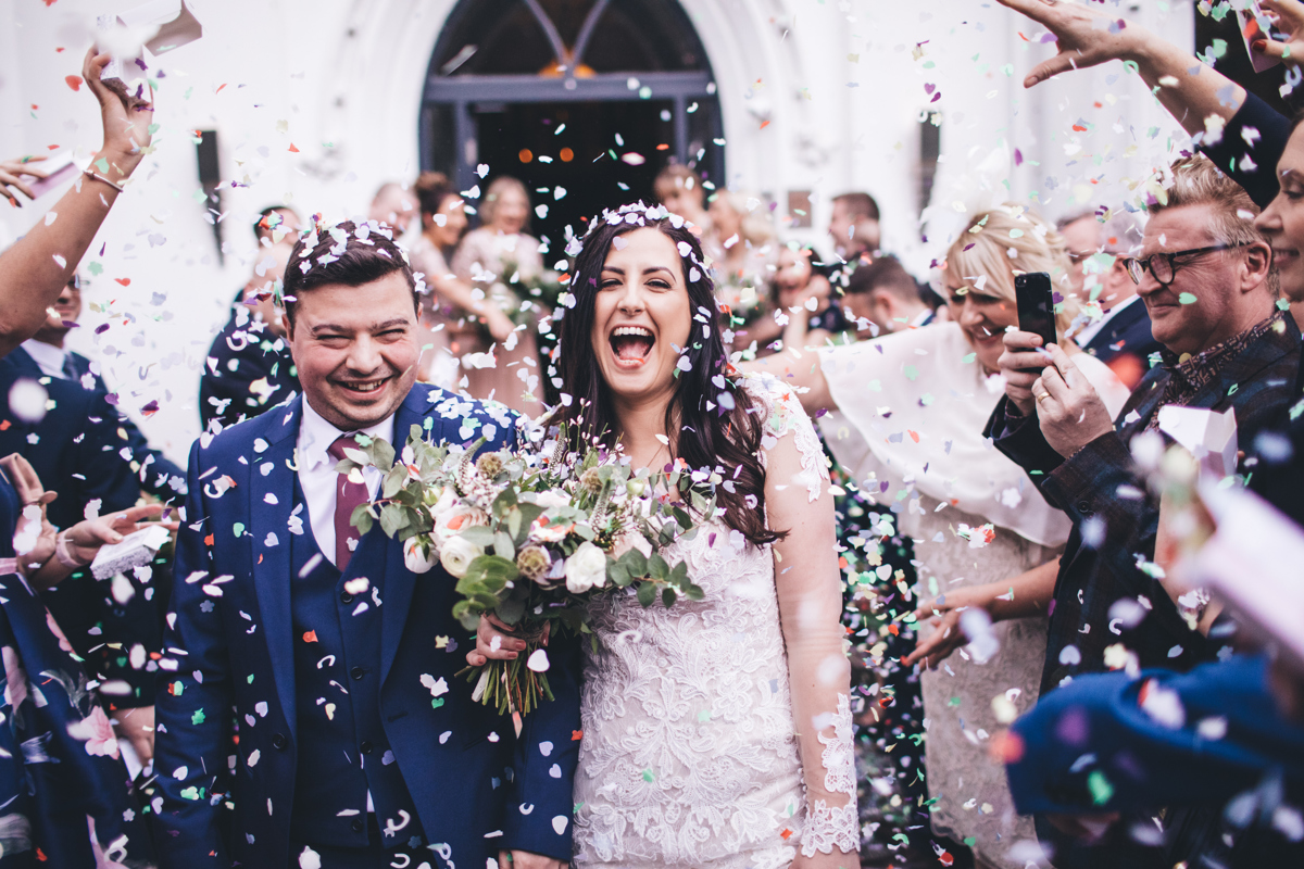 Bride and groom getting covered in confetti as they walk past their wedding guests either side of them