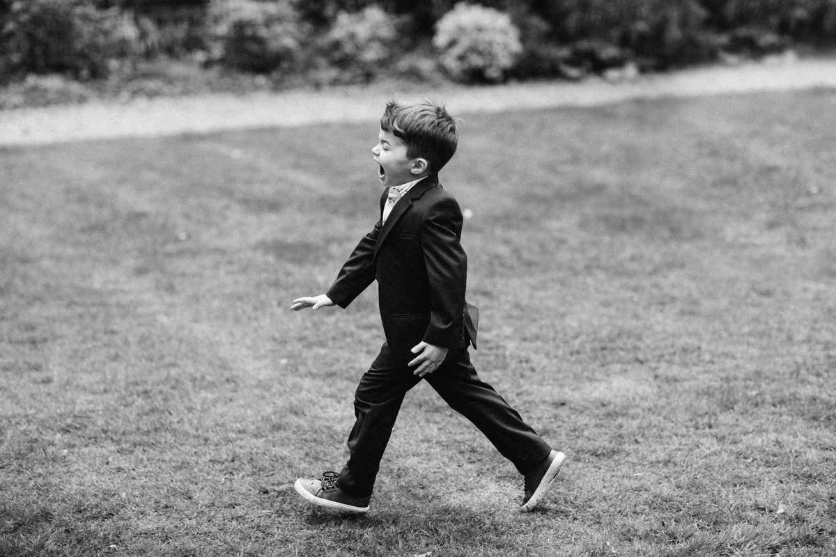 Black and white photograph of a young boy wearing a suit running across a lawn with his mouth open