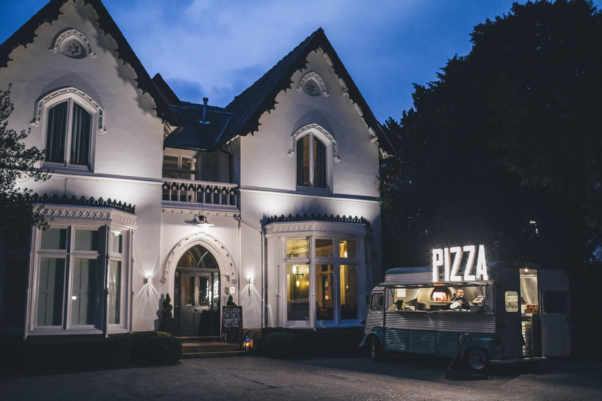 An evening shot of a pizza van with large lit up 'Pizza' sign in front of Didsbury House Hotel