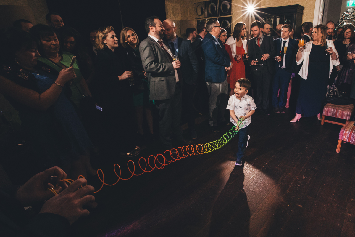 Young boy on the dancefloor holding one end of a rainbow coloured slinky which is being stretched whilst adults are stood in the background