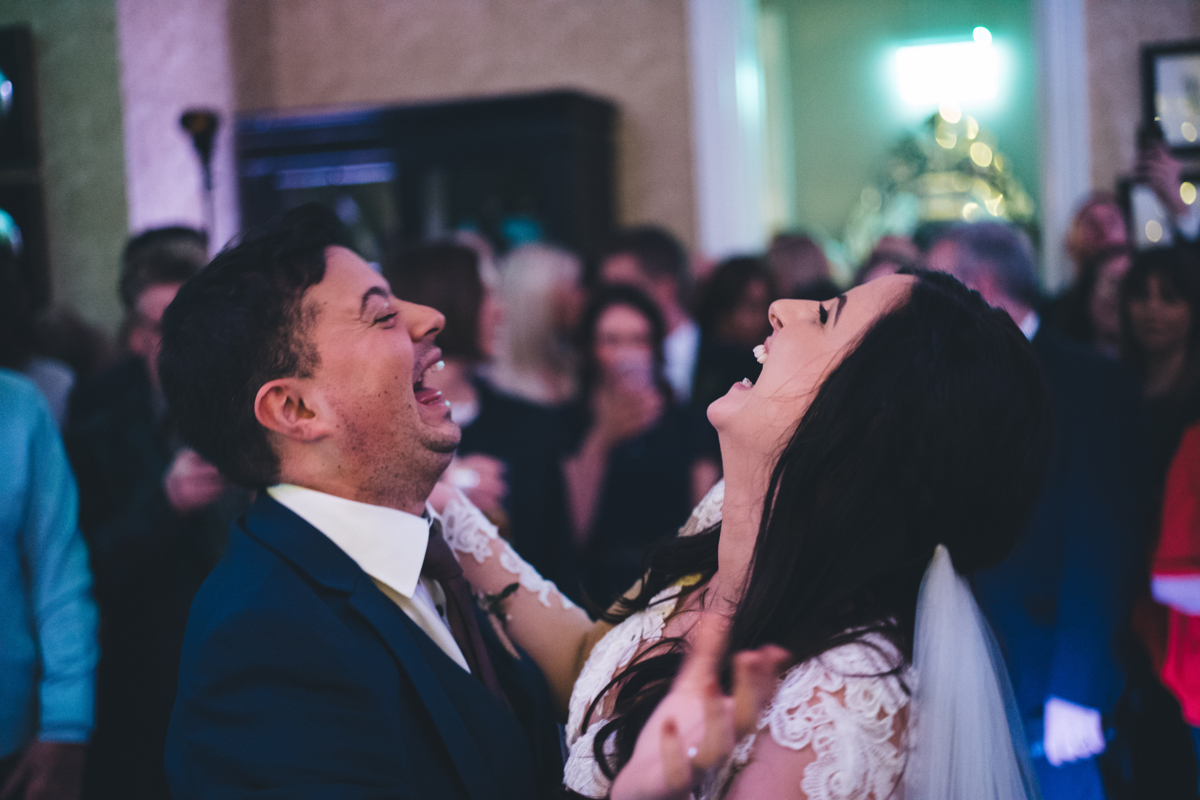 Bride and groom on the dancefloor facing one another laughing with their faces pointing upwards