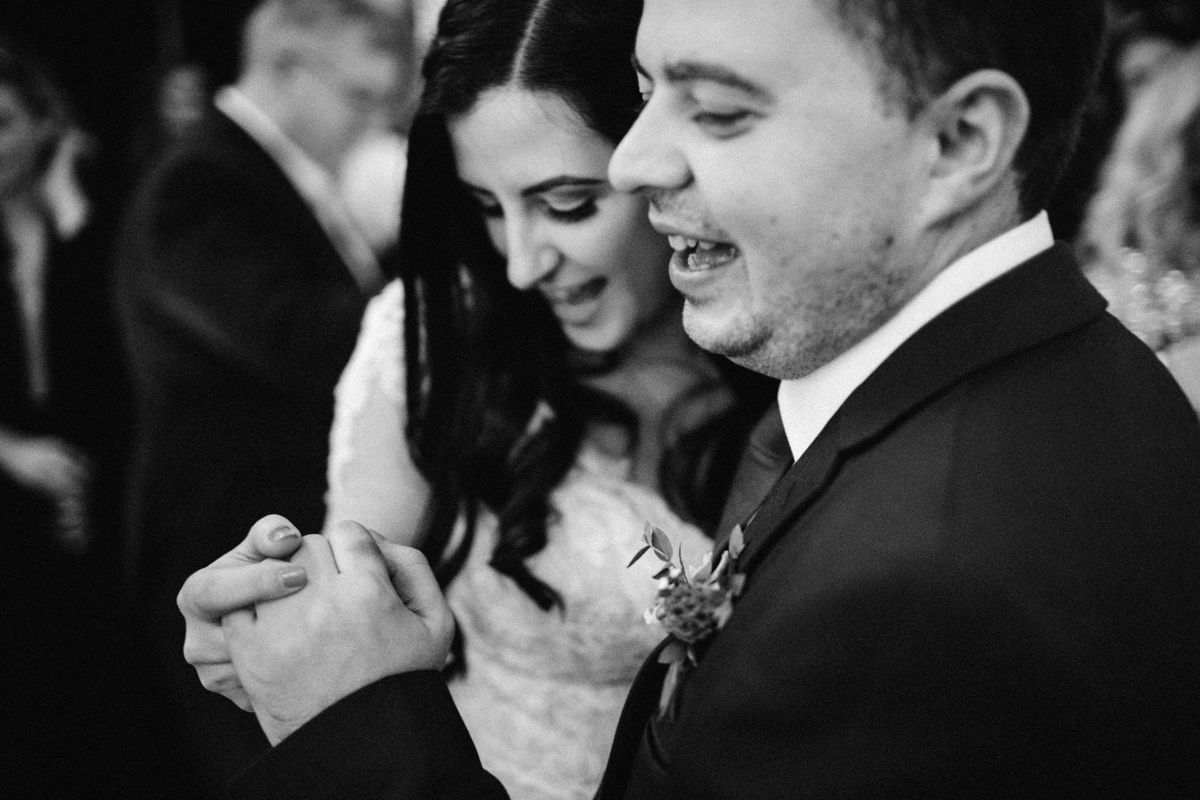 Black and white photograph of the bride and groom holding hands dancing