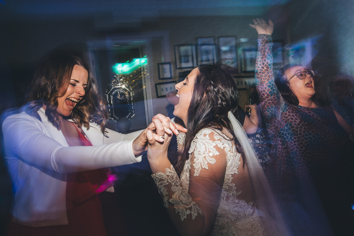 Bride dancing with a female friend, both have their mouths open as they sing along to the song
