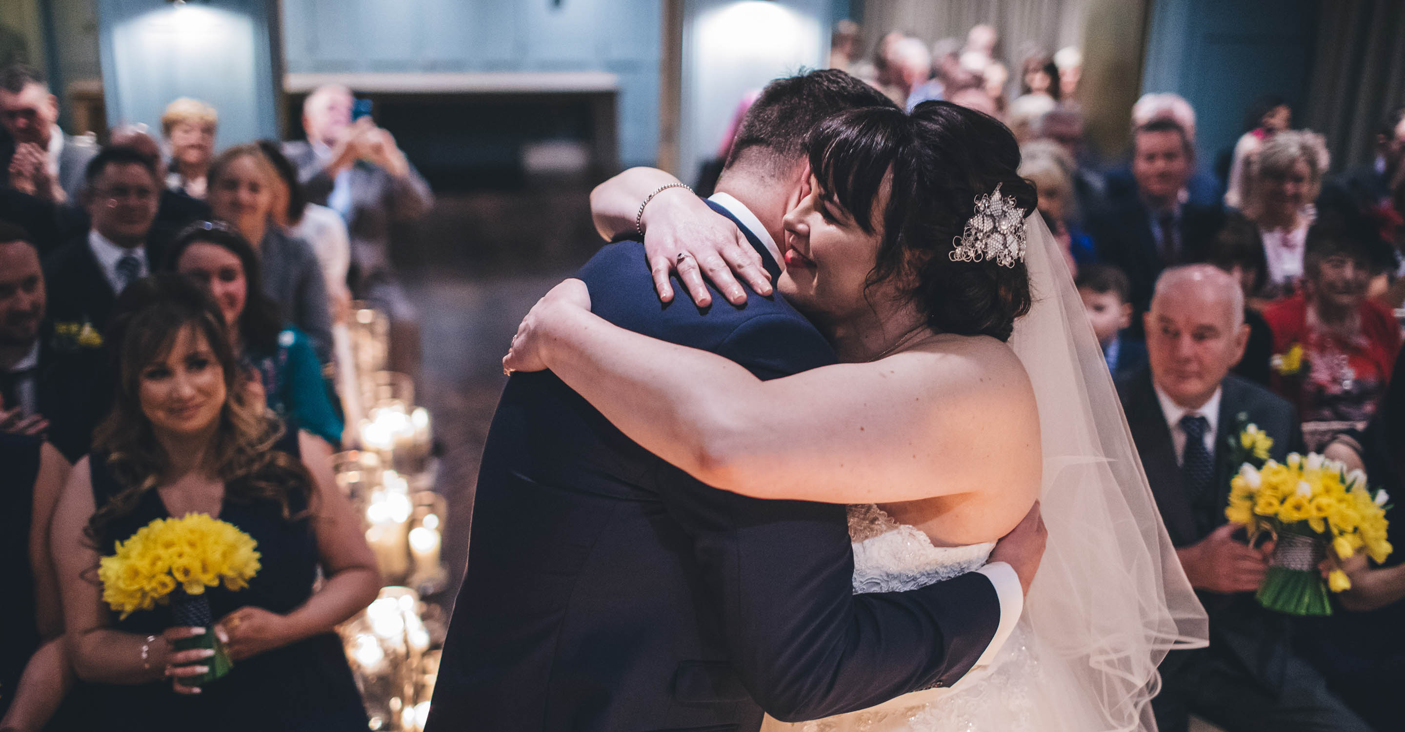 Bride and groom hugging each other at the top of the aisle with the wedding party in the background