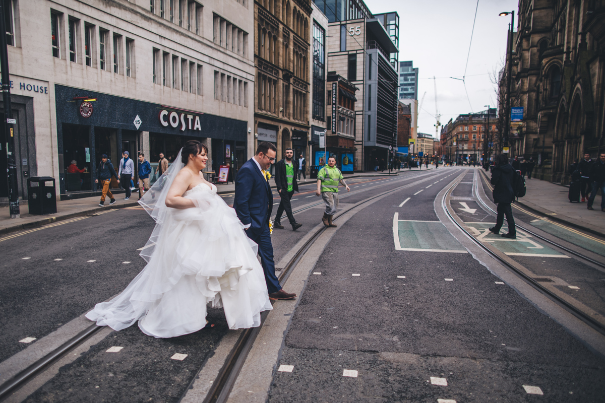 Bride and groom crossing tram tracks next to the Town Hall in Manchester