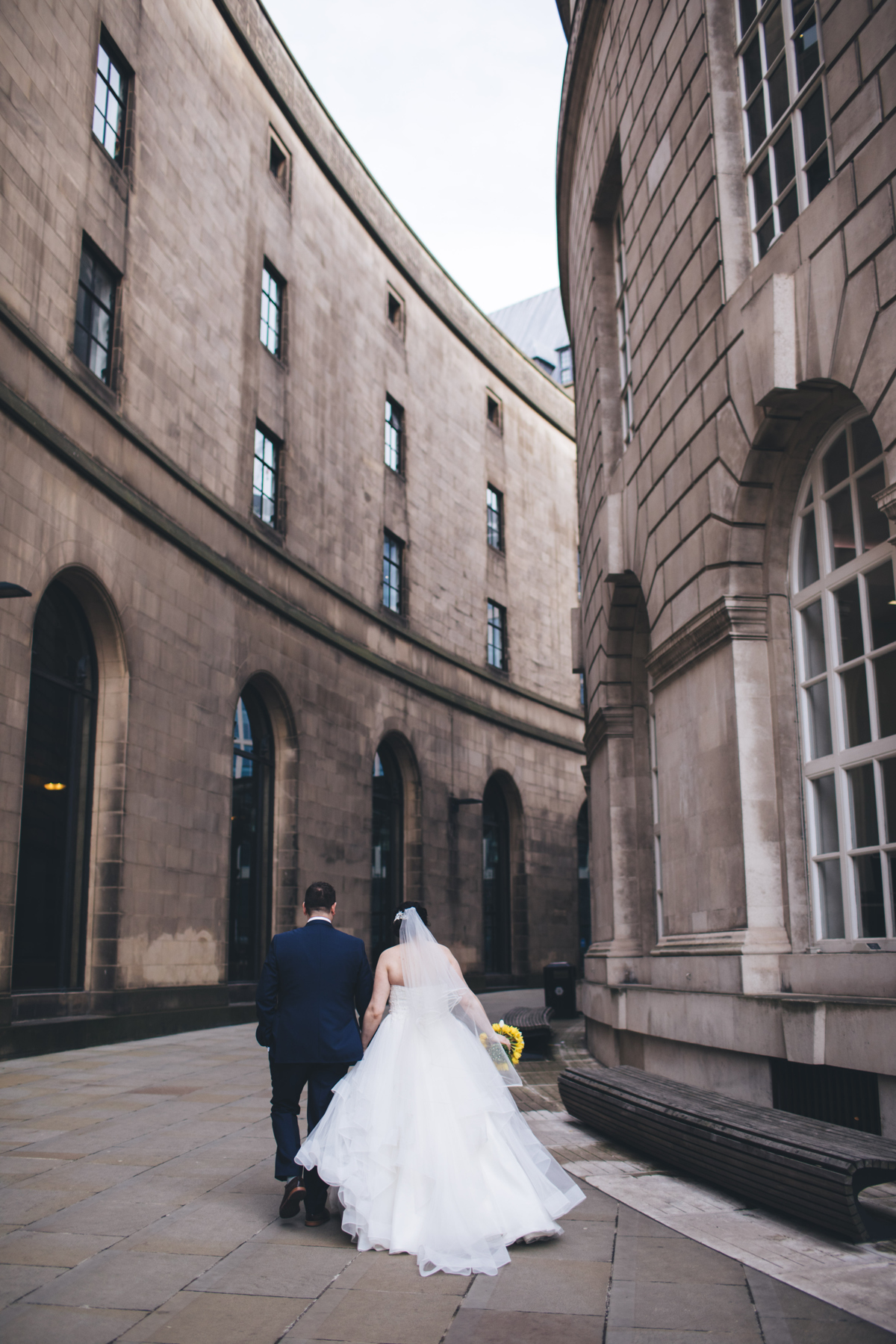 Bride and groom walking away from the camera next along a curved walkway next to the Central Library in Manchester