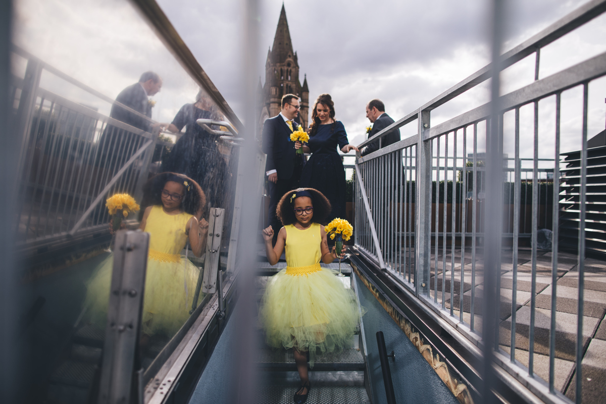 Flowergirl dressed in yellow holding a bouquet of Daffodils walking down the stairs from the rooftop at King Street Townhouse in Manchester