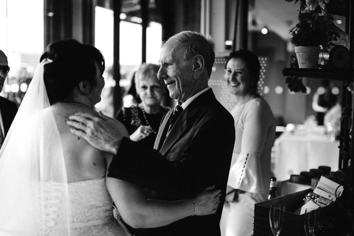Black and white photograph of bride with her arm around an elderly gentleman who has his hand on her shoulder