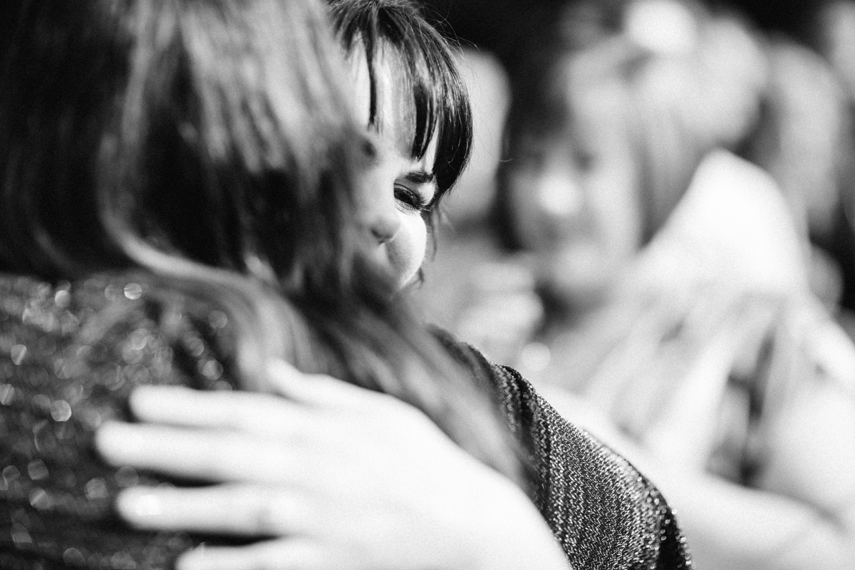 Black and white photo of bride hugging one of her guests with just a glimpse of the bride's face in focus