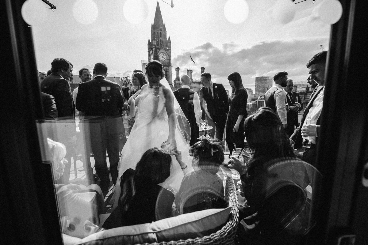 Black and white photo through a window towards the terrace at King Street Townhouse Manchester with the bride in the centre of the shot and other wedding guests chatting on the terrace