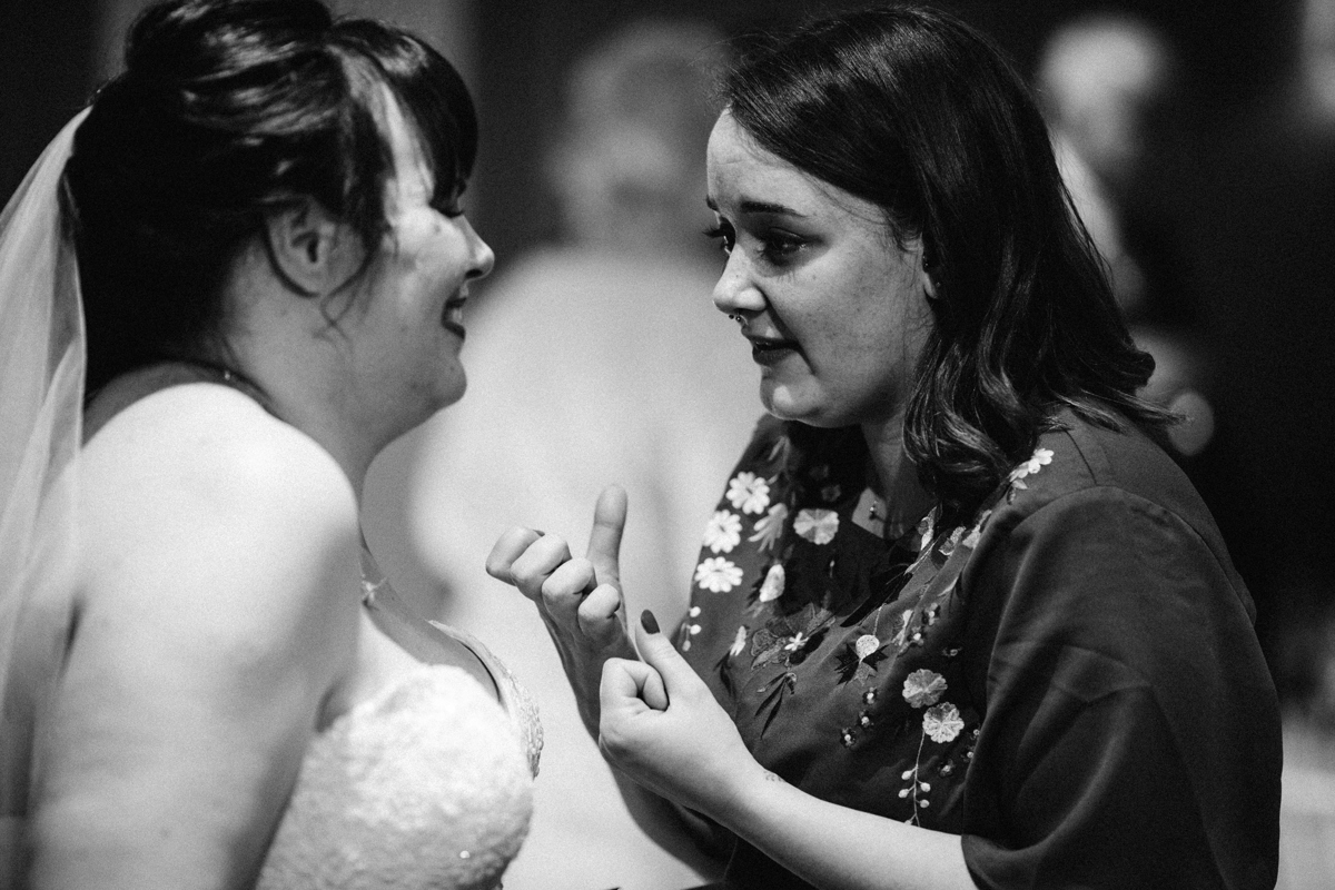 Black and white photograph of the bride smiling chatting to a woman in a floral patterned dress in front of her
