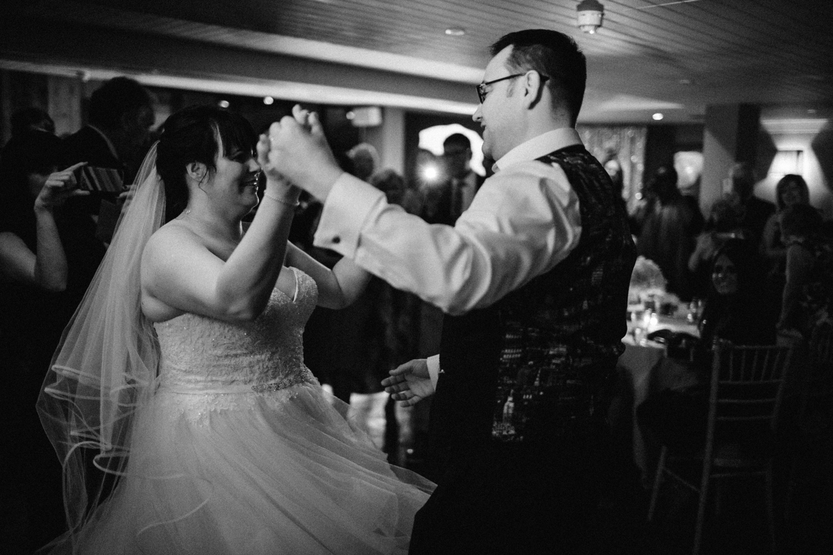 Black and white shot of the bride and groom dancing holding hands