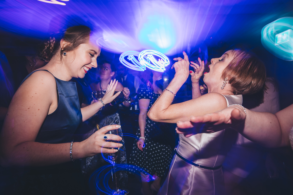 Two female wedding guests with their eyes closed dancing with their arms and hands up