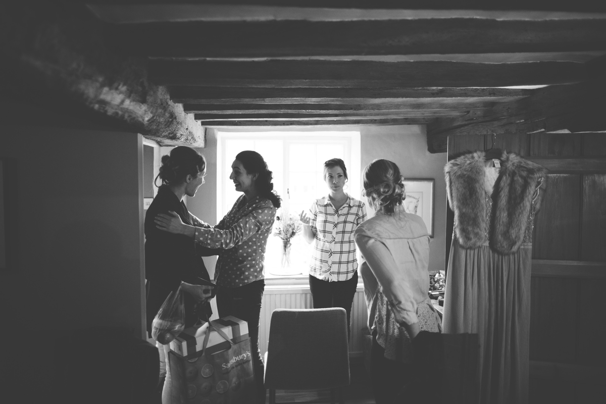 Black and white photograph of four bridesmaids wearing their own clothes in a room with a low wooden beamed ceiling